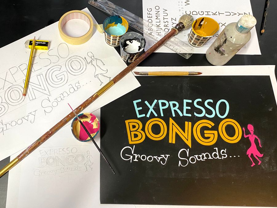 An Expresso Bongo chalkboard sign in progress, with brushes, mahl stick and paint alongside