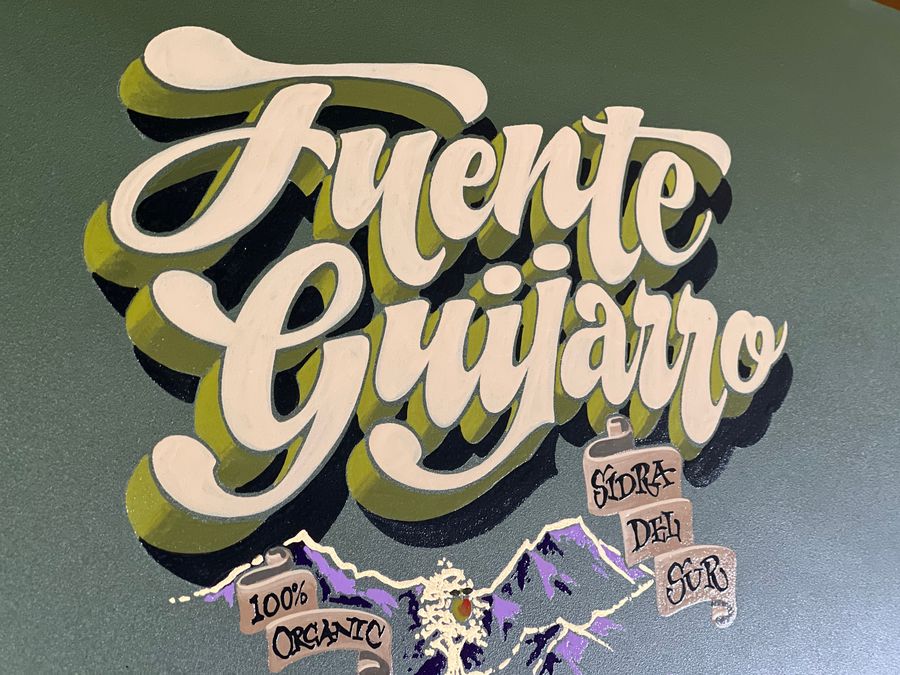 Fuente Guijarro lettered in ornate cream script with olive shading on a grey-green panel