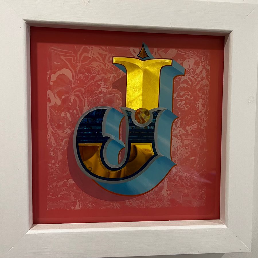 A gilded and shaded letter on a red damask ground, in a white box frame