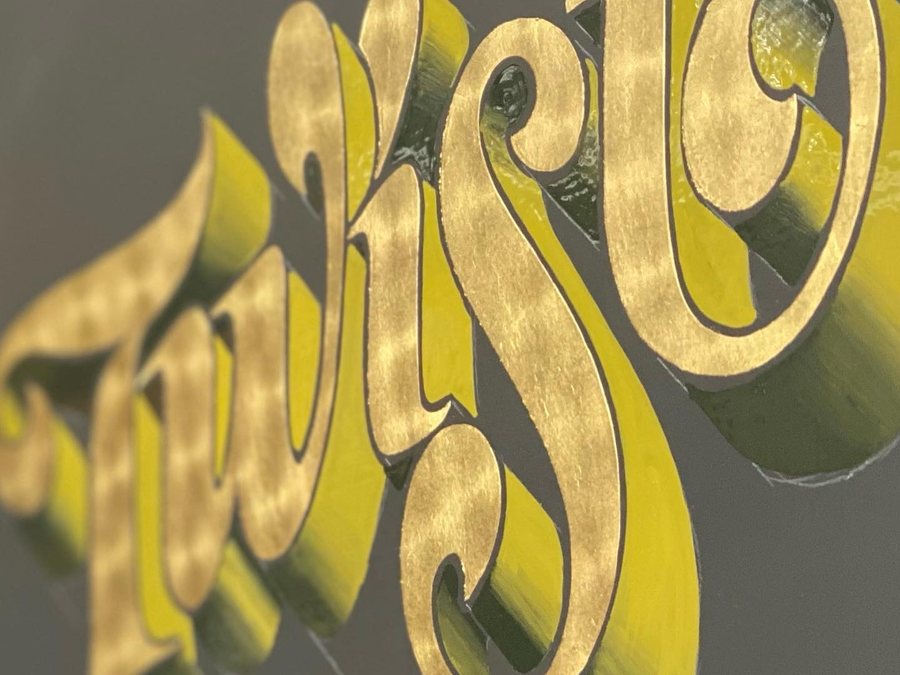 Script lettering reverse gilded on glass, the bright gold set against a matte ground