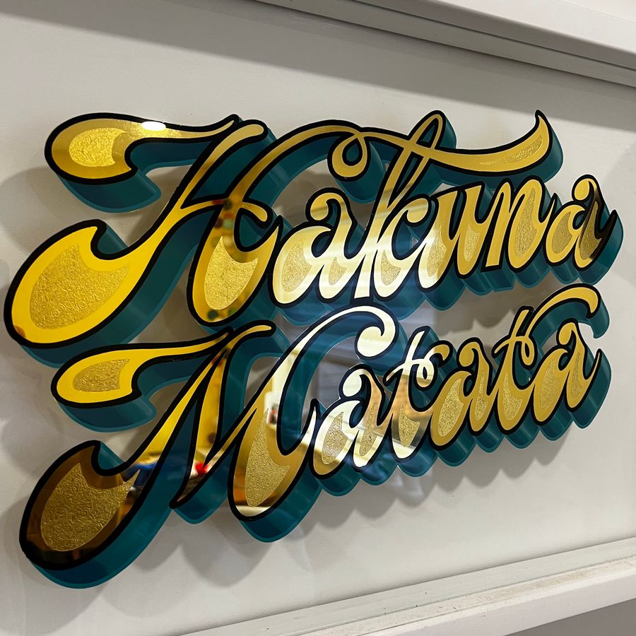 Hakuna Matata in gilded script with a teal shade, framed on the wall