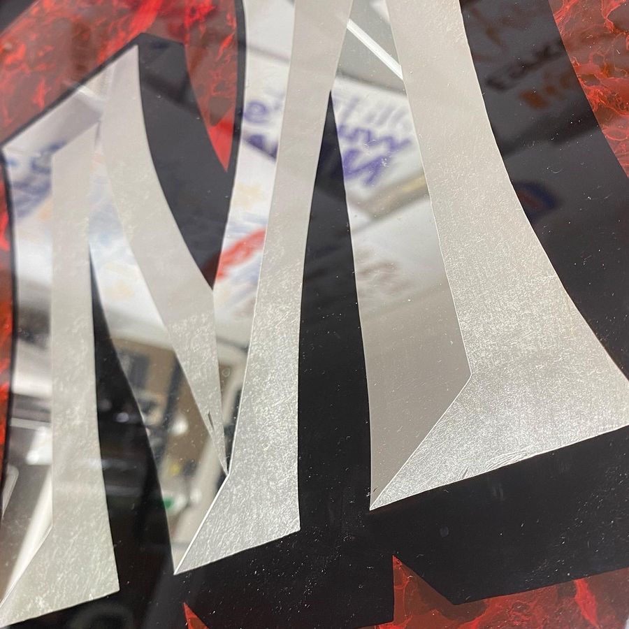 Aluminium leaf letters laid on glass over a red patterned ground, part-way through a reverse gild
